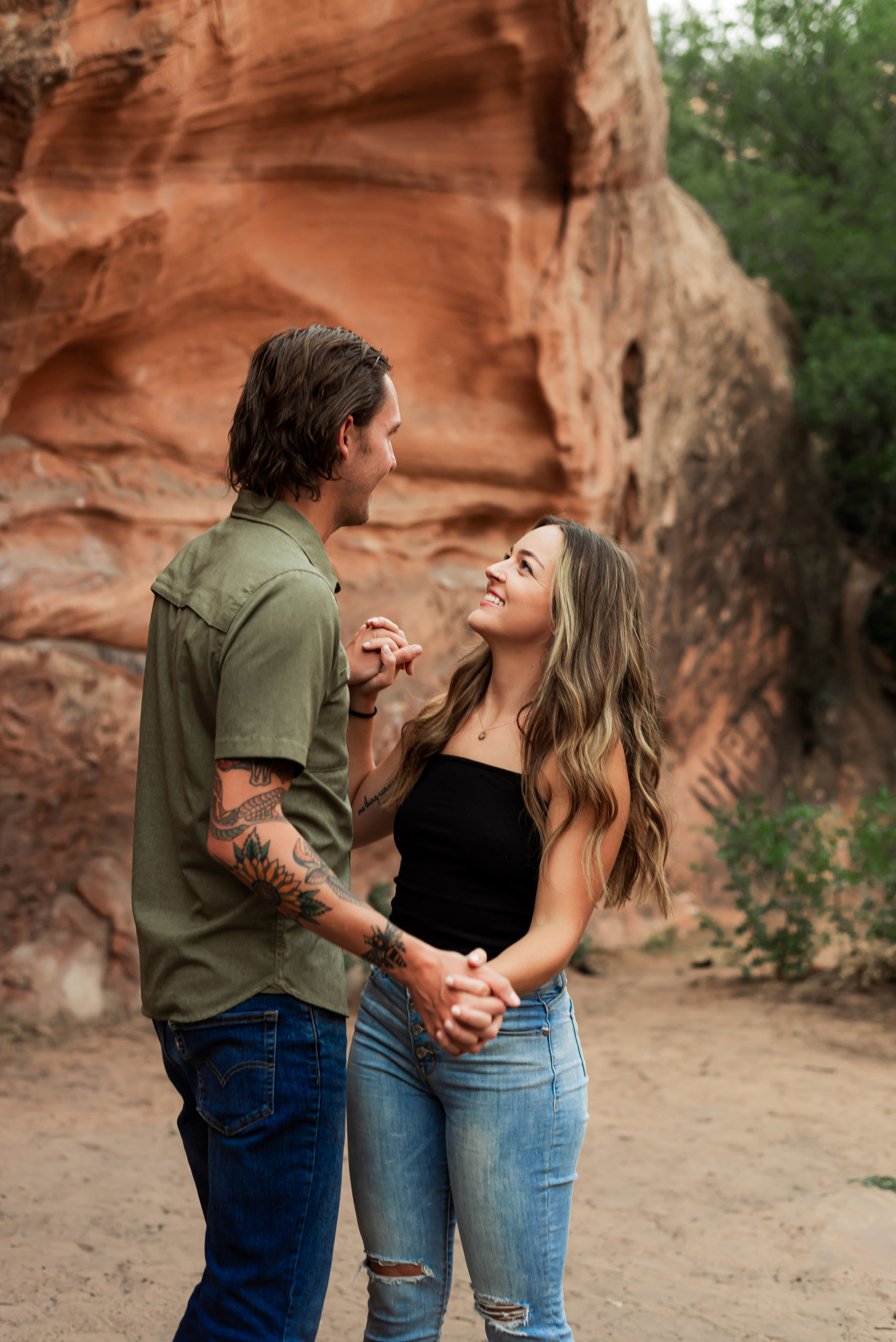 couple holding hands smiling at each other in front of utah red rock landscape