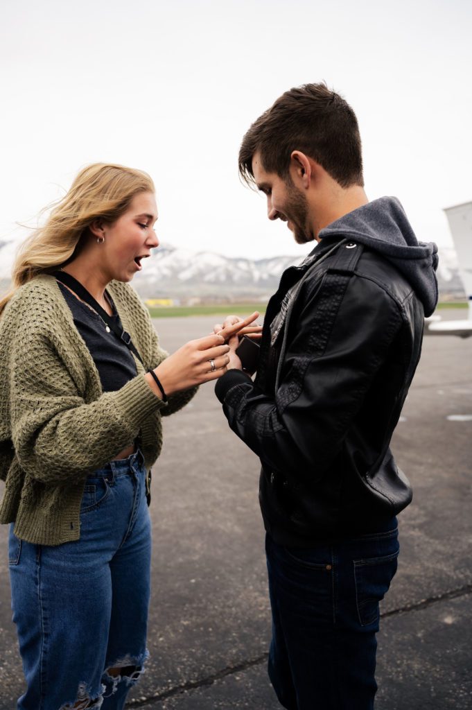 Pilot puts engagement ring on fiance's finger after surprise airport proposal in Logan, Utah.