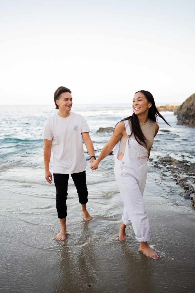 Laughing couple runs around at Laguna Beach engagement session.