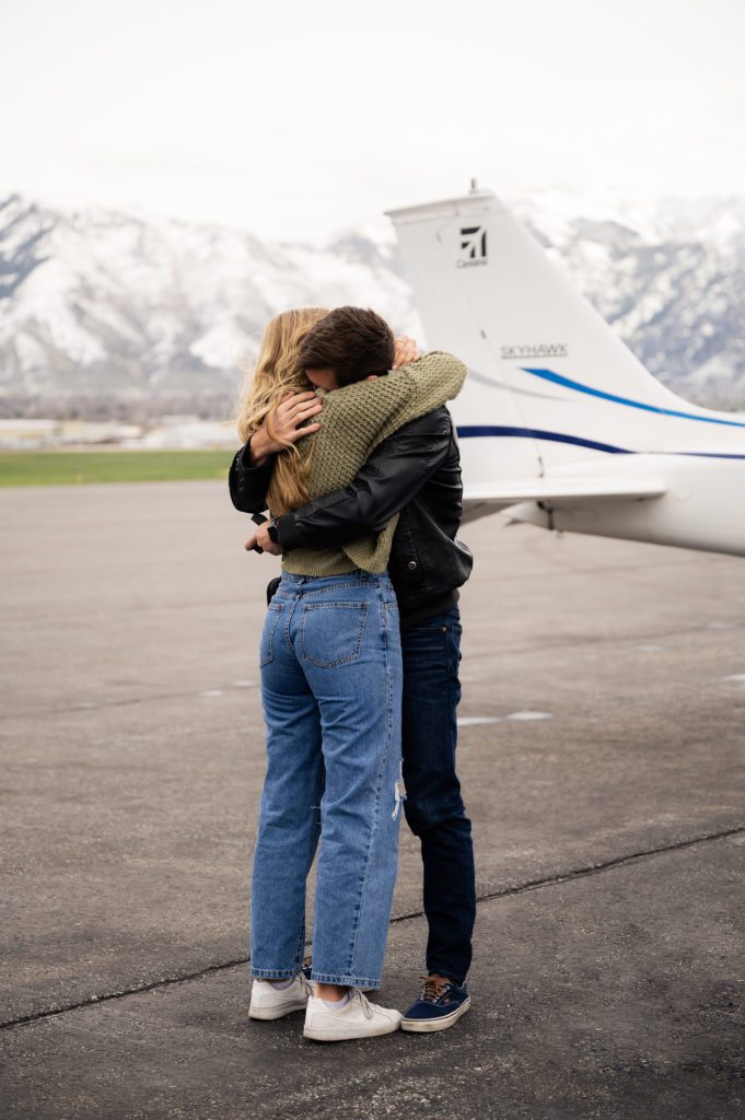 Engaged couple hugs after surprise airport proposal.