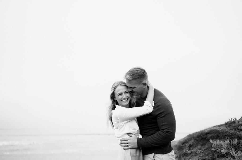 Black and white candid photo of an engaged couple during half moon bay engagements with san francisco, california wedding photographer and videographer team.