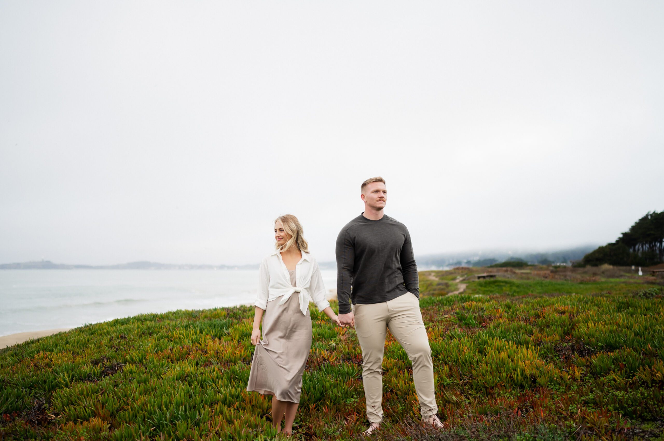 Engaged couple pose casually barefoot for engagement photoshoot in Half Moon Bay, San Francisco, California with destination wedding photographer and videographer team.