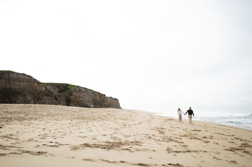 half moon bay engagements couple holding hands walking along the beach