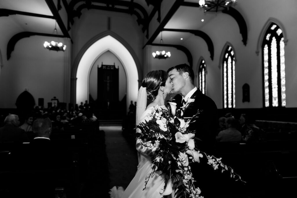 Bride and groom kiss at the end of the aisle after New York city church wedding.