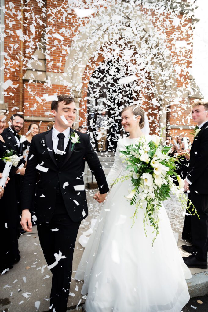 Bride and groom walk through confetti exit outside Park Presbyterian church in Syracuse New York.