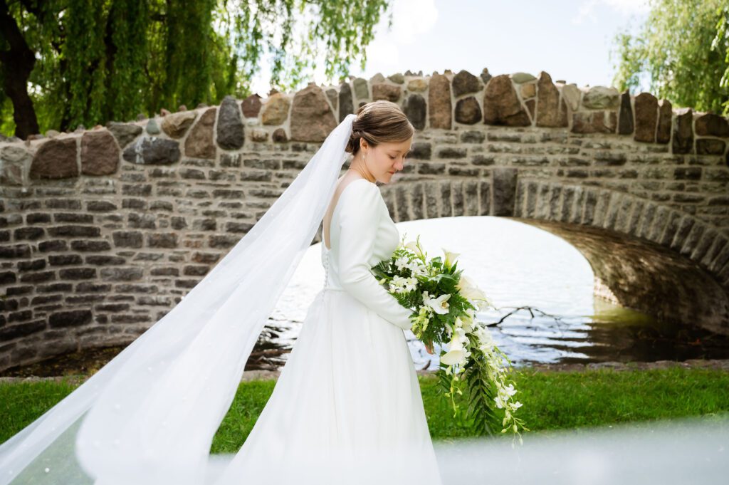 Bride standing with bouquet at Syracuse park bridge.
