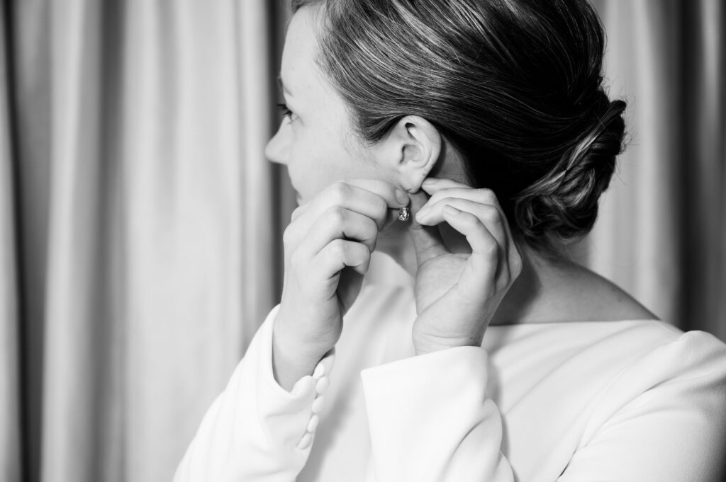 Bride puts in earrings while getting ready for Marriott Syracuse downtown wedding day.