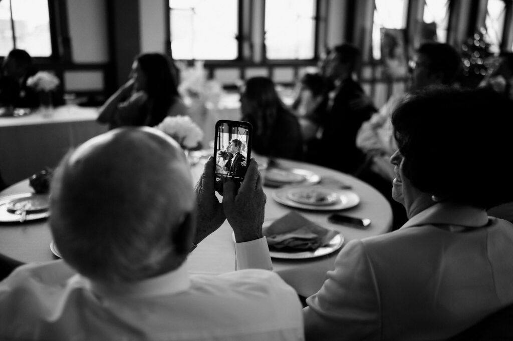 grandpa takes photo of bride and groom sitting together during wedding dinner in brigham city utah
