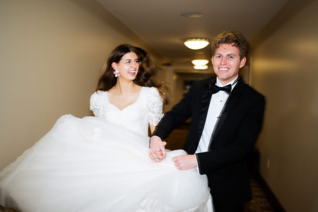 bride and groom run down hallway of hotel venue brigham academy center in their wedding attire