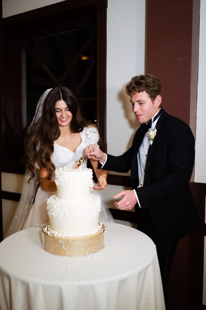 bride and groom cut white tiered pearl cake at utah venue brigham academy center in their wedding attire
