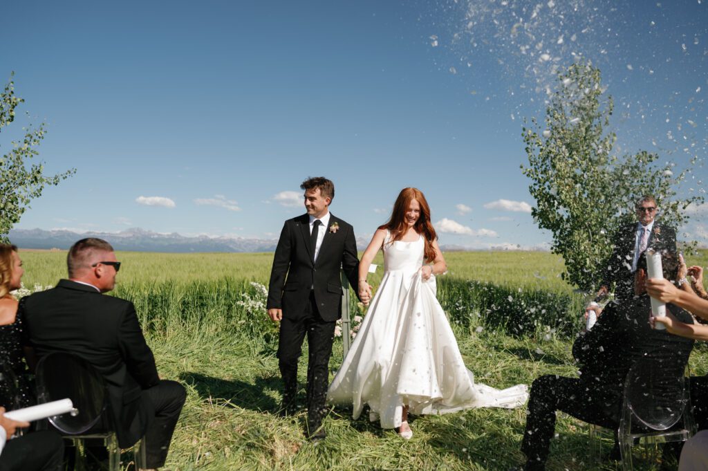 couple exits aisle of wedding ceremony in jackson wy with confetti poppers