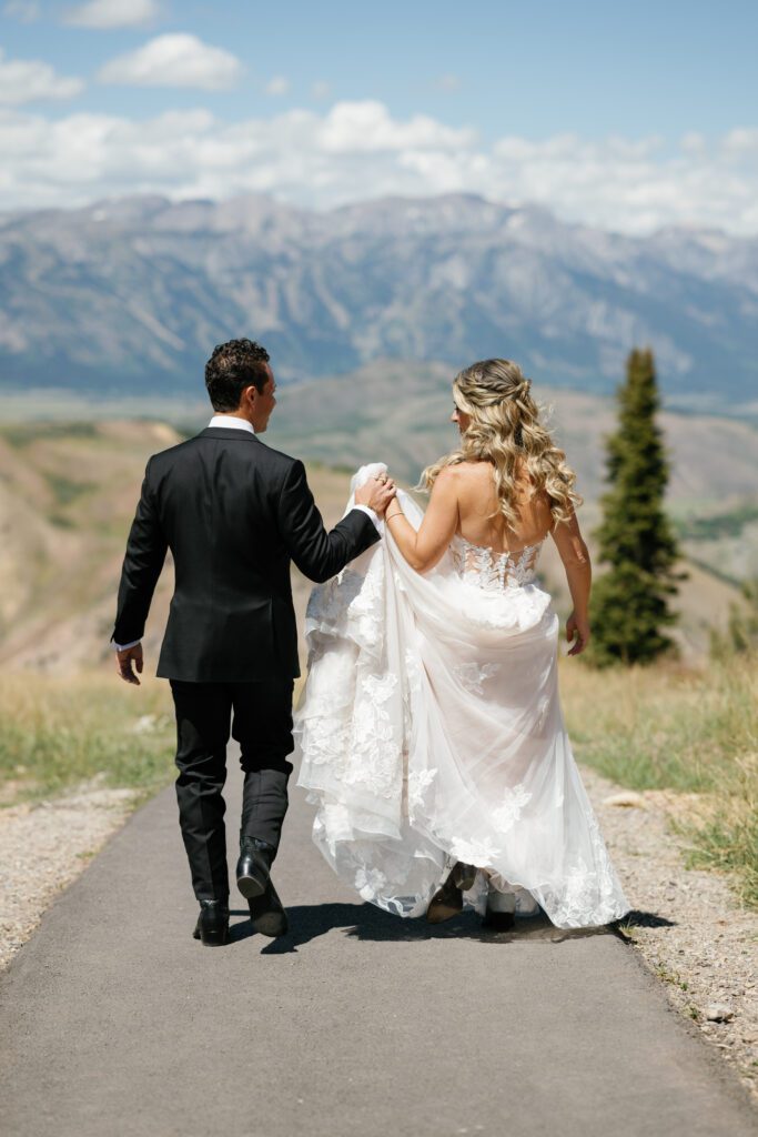 Couple holding hands with mountains backdrop during Snow King Jackson Wyoming wedding