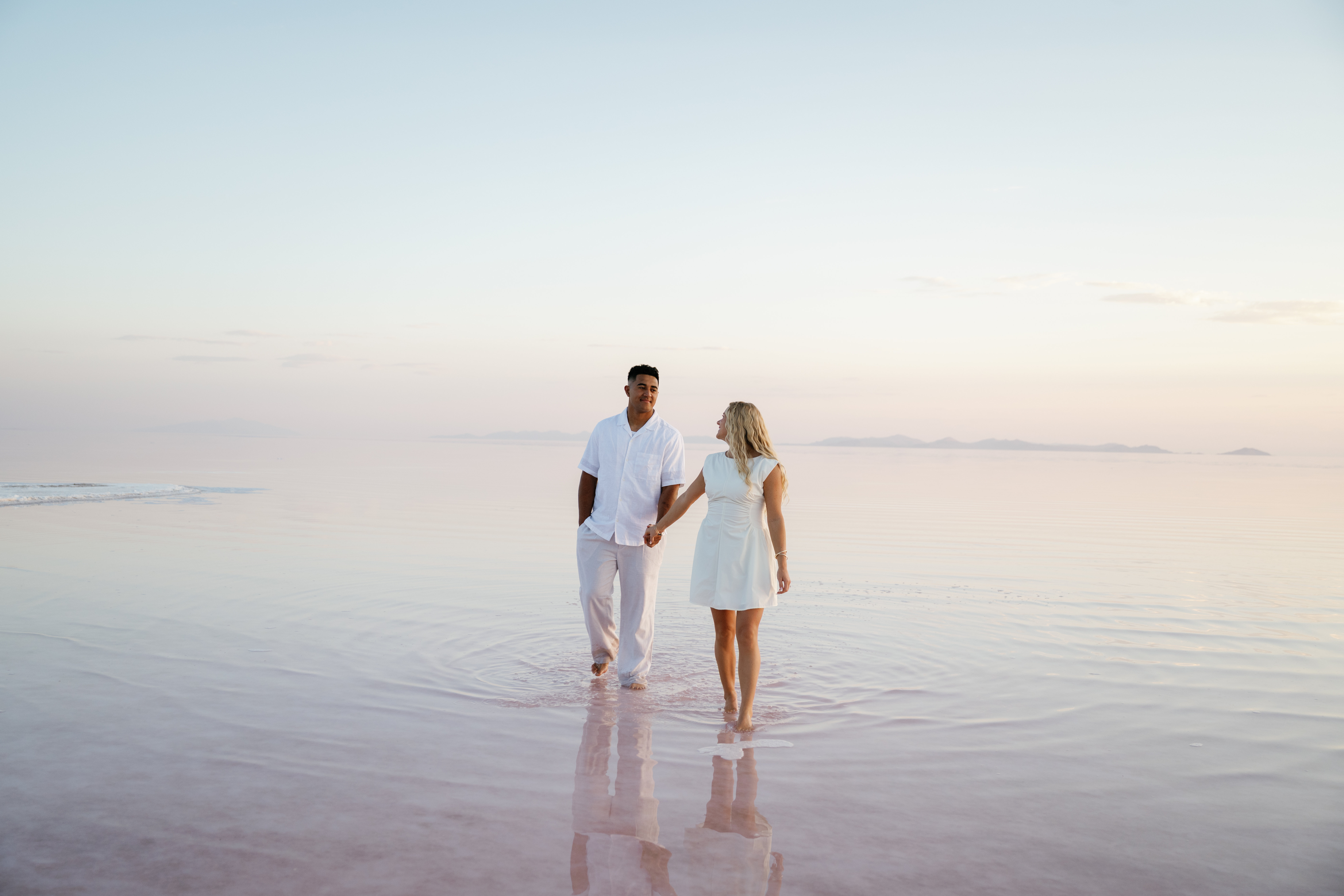 A couple holding hands on the beach during Utah pink lake engagement photo shoot