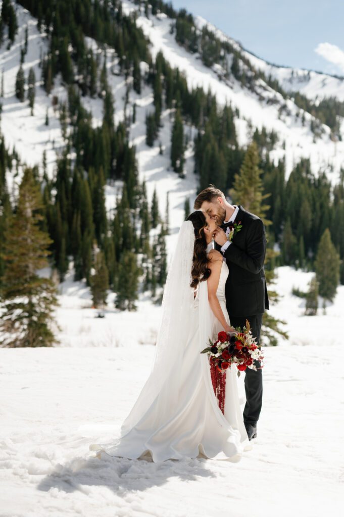 The couple kissing with the mountains in the background during winter wedding Snow Pine Lodge at Park city