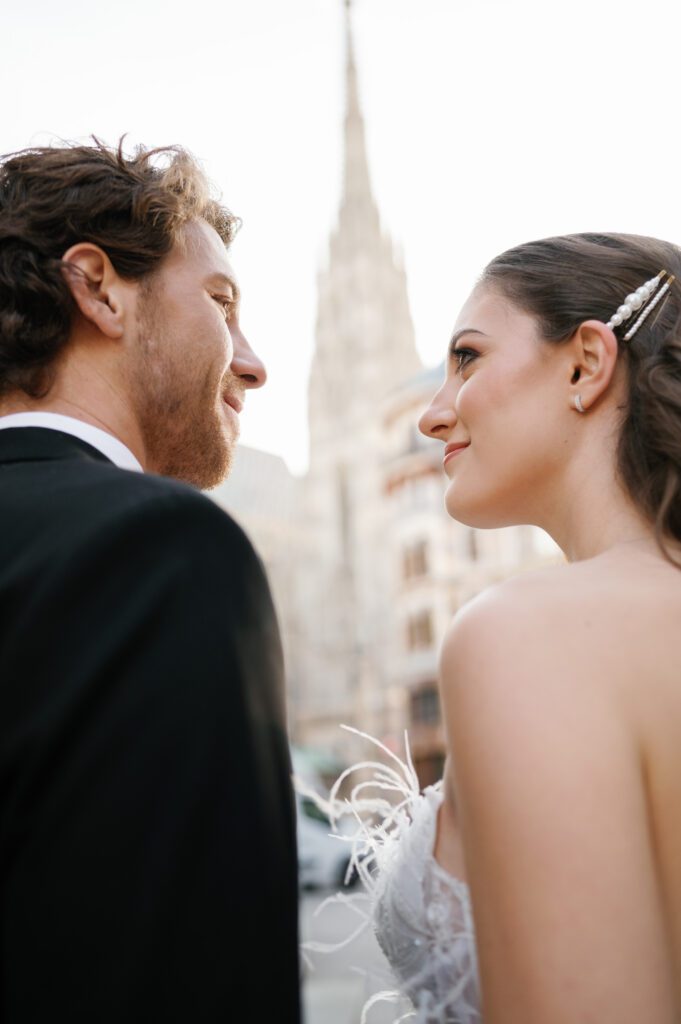 A close-up shot of bride and groom looking at each other with venue building in the background captured by Vienna wedding for Photographer
